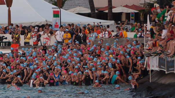 Close-up crop of the previous image - I am on the front row of people entering the water, with both hands adjusting my goggles. Black suit, blue cap.