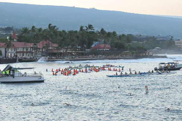 People lining the entire length of the ocean wall up and past the 'Kona Inn'. The safety kayak/paddle-boards await the swim start.